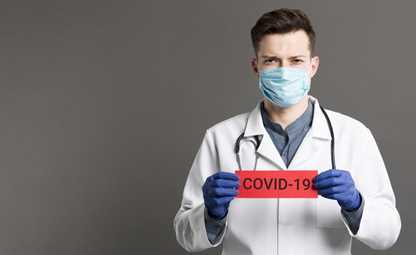 A doctor wearing a mask and gloves holding a piece of paper with COVID-19 written on it
