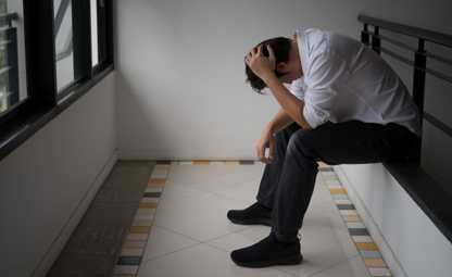 An upset and stressed man sitting on a balcony