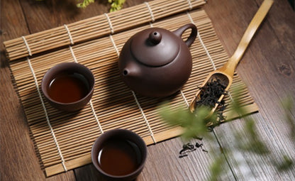 Two cups filled with black tea next to brown teapot and a wooden spoon