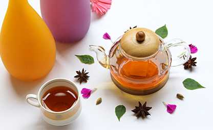 A kettle and a cup filled with herbal tea raw herbs and spices