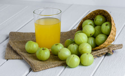 Organic amla fruits tossed over a jute bag from a wooden bowl next to amla juice in a glass