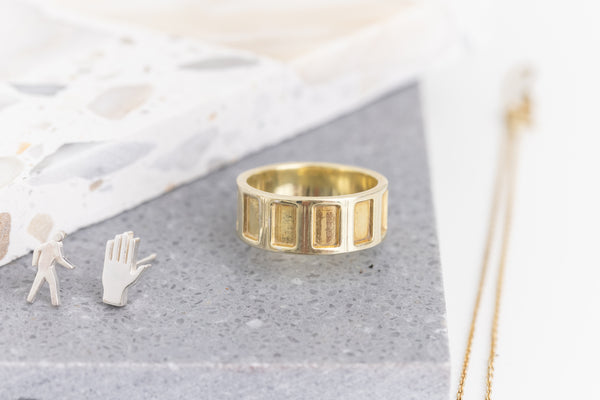 The 18k Gold Vermeil Concrete Waffles ring showcased on grey tile, with the silhouette of the Crosswalk studs to the left, capturing the essence of urban design in jewelry.