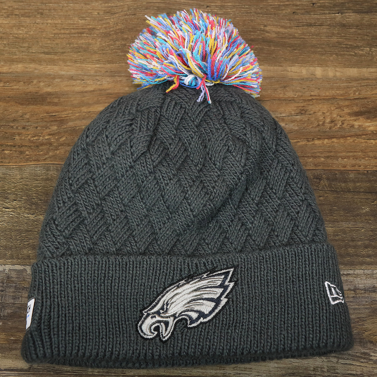 The front of the Women's Philadelphia Eagles On Field NFL Crucial Catch Intercept Cancer Patch Rainbow Pom Pom Winter Beanie | Graphite Gray Winter Beanie