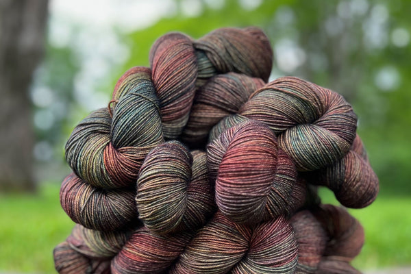 Stack of colorful yarn, in moody shades of greens, reds and oranges, with blips of brighter specks due to Signature Ply technique. 