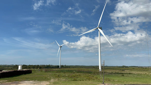 Two windmills set in a large field, with deep blue skies and wispy clouds above.