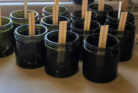 Empty green glass jars with wooden wicks ready to pour candles.