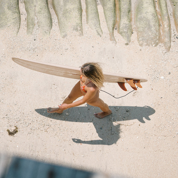 Female surfer walking with her surfboard, photo taken from above at the beach