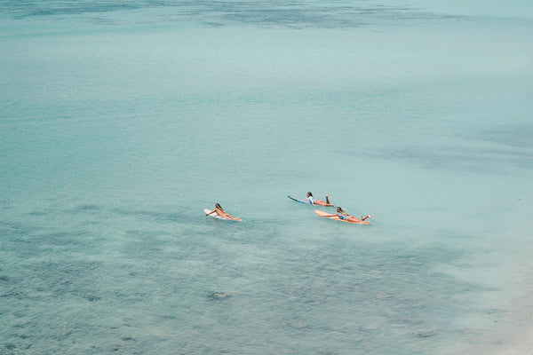 three surfer girls paddling out in the clear blue ocean of Lombok