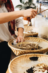 A lady using traditional counterbalance hand scales to dispense a herbal prescription into wicker trays at The Grove Chinese Medicine