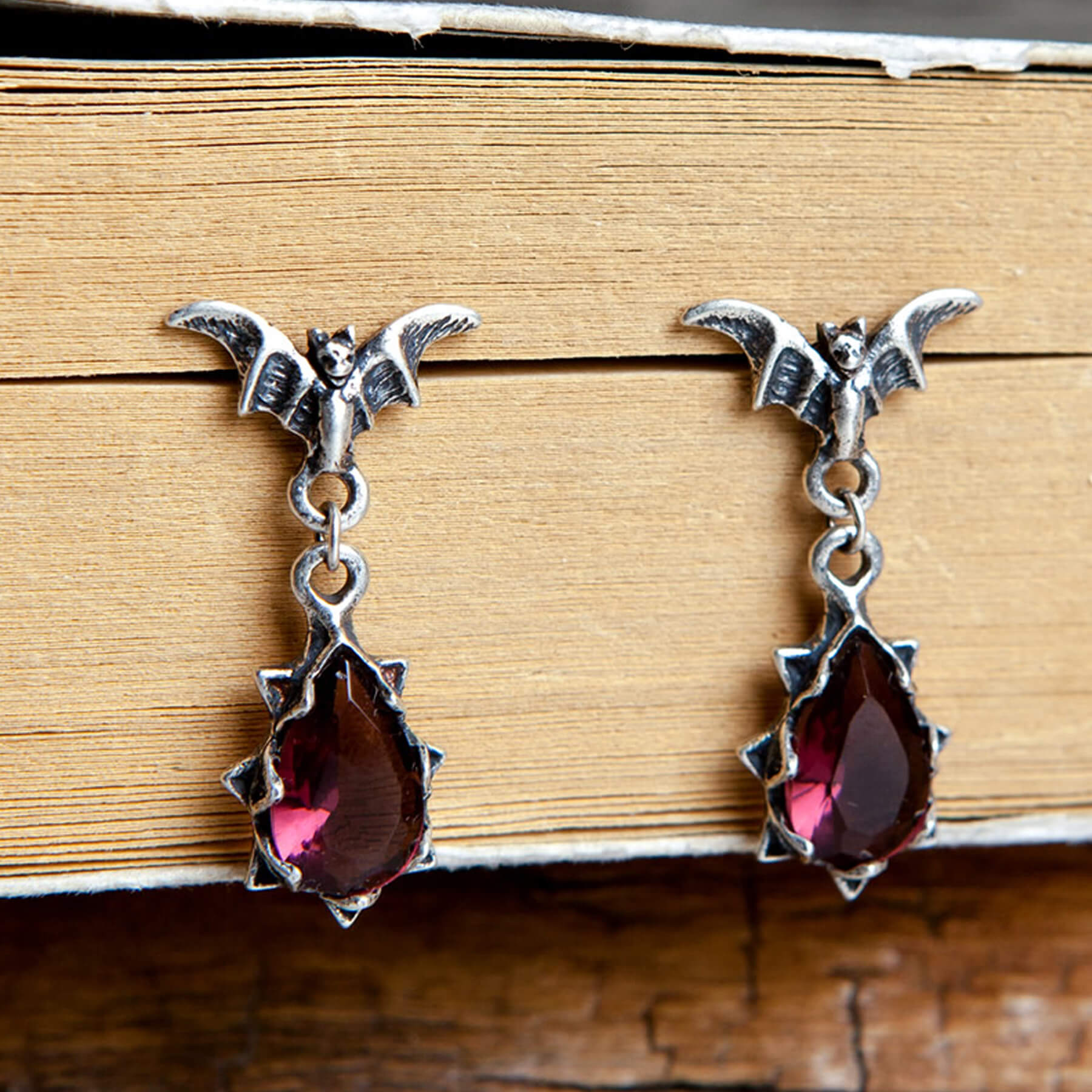 close-up-of-two-gothic-bat-earrings-with-ruby-gemstones-in_a_book_JECJ007