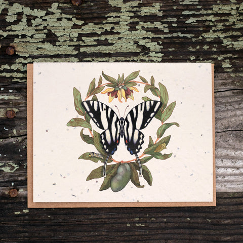 A photo of a Bower Studio Seed card featuring an illustration of zebra swallowtail . The card is laying on weathered wood with lichen growing on it