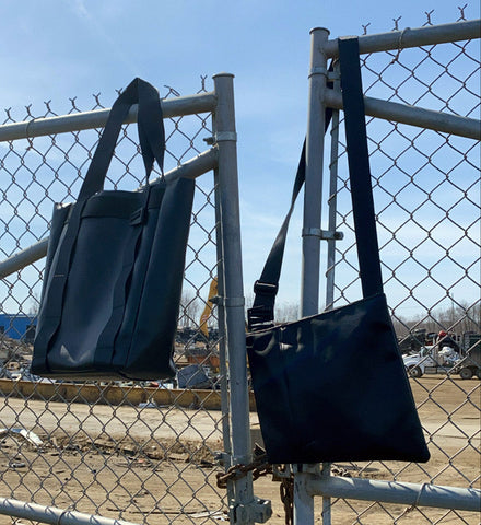 Bags made with seatbelt straps hang from a fence in a scrapyard