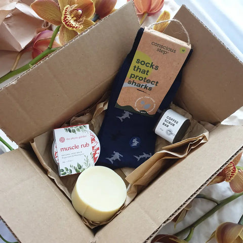 Cardboard box filled with products including socks, muscle balm, coffee scrub and shave soap.