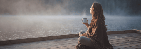 A woman enjoying a hot drink by a lake in nature