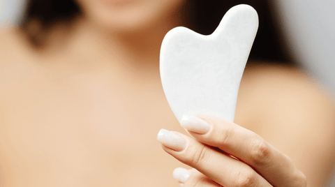 A woman holding a white heart-shaped gua sha tool in her hand.