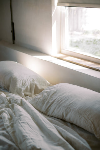 Undone bed with white sheets in morning light | Jenny Nordic Skincare