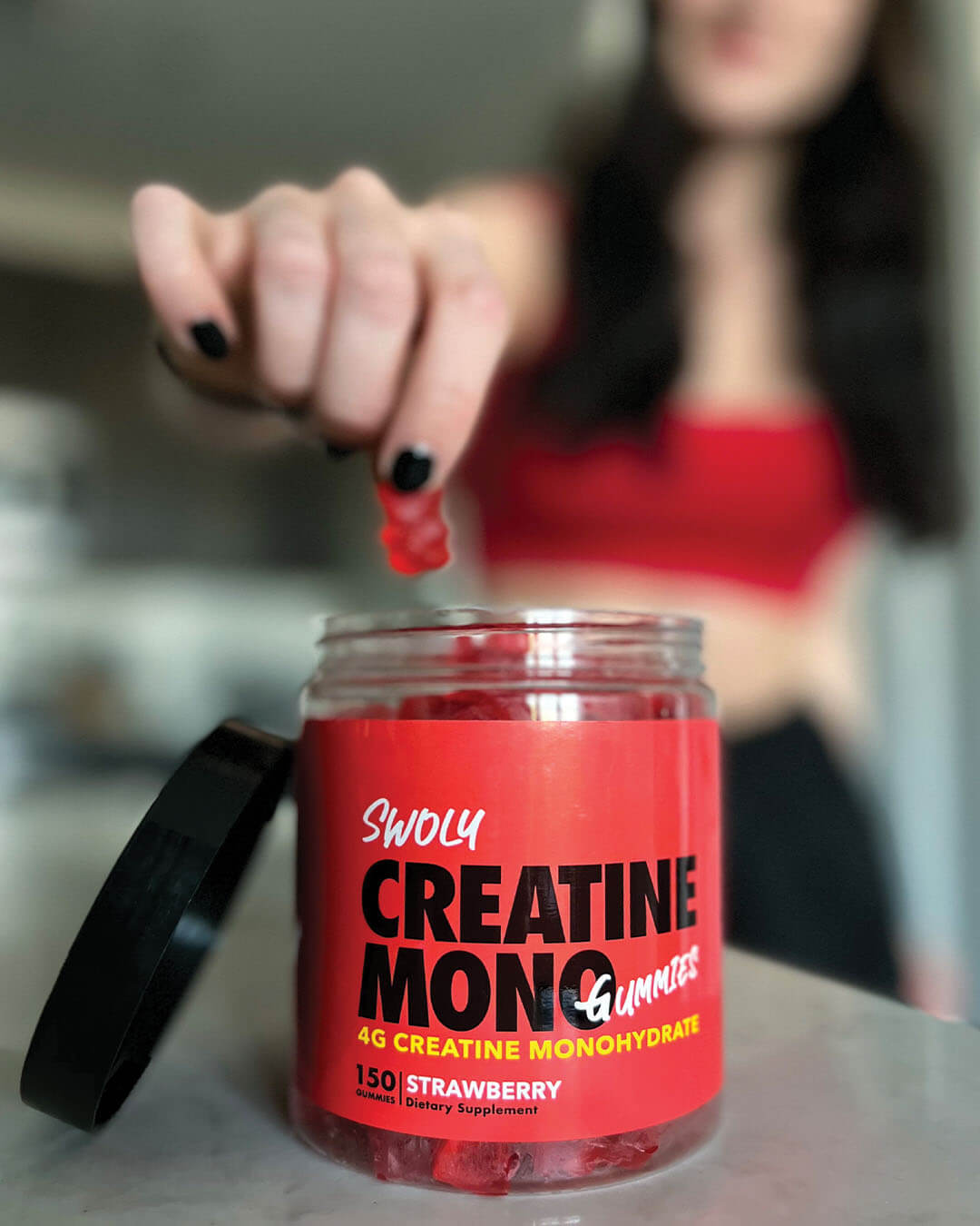 hand grabbing swoly creatine gummies from container in a gym, strawberry flavored gummy supplement