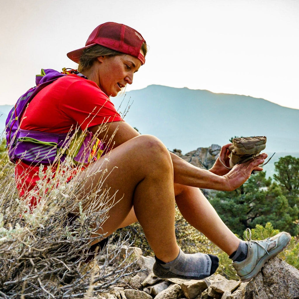 a trail runner wearing Ridge Rock Creek Low Cut Socks sits on a rock to pour pebbles out of their running shoe