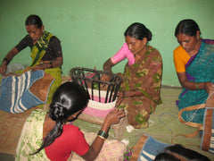 A group of rural Indian women sitting on workshop floor making jute and cotton baskets.