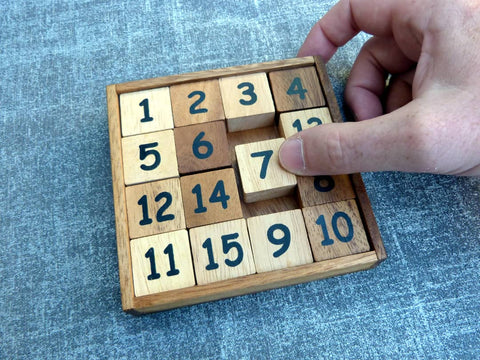 Schiebespiel aus Holz in einem Holzrahmen mit 15 quadratischen Teilen die von 1 bis 15 nummeriert sind.