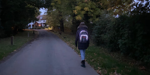 Young woman walking along a lane wearing a lit up Futliit LED backpack