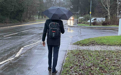 Commuter with an umbrella wearing a Futliit LED backpack in heavy rain