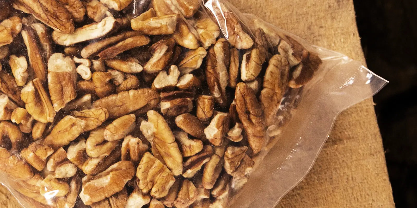 Clear plastic bag of raw pecan pieces on a wood table