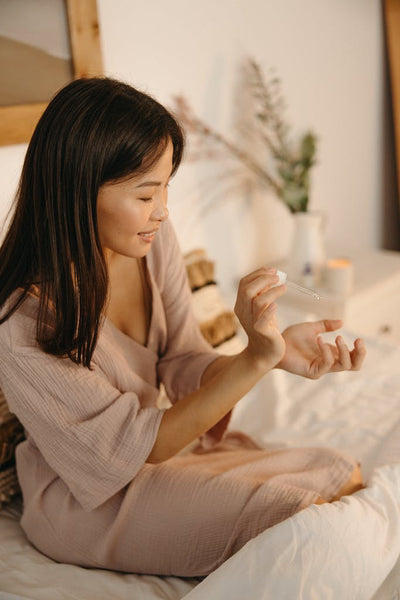 Young woman sitting in bed applying body oil.