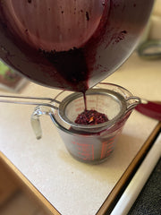 last bit of elderberry and herb juice straining through fine mesh metal strainer into liquid measuring cup