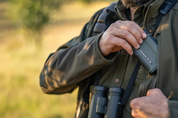 A man placing a Leica Rangemaster CRF PRO into his hunting jacket pocket.