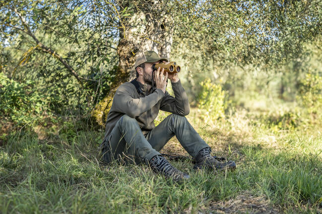 A hunter using the Leica Geovid Pro 10x42 AB+ while seated in the bush.