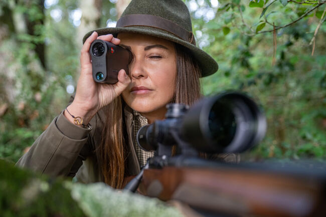 A huntress using a Leica Rangemaster CRF R for precise distance measurement.