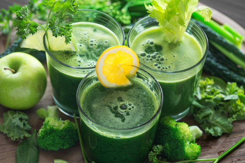 Three glasses of green juice surrounded by kale, bell peppers, green apple, and other green vegetables