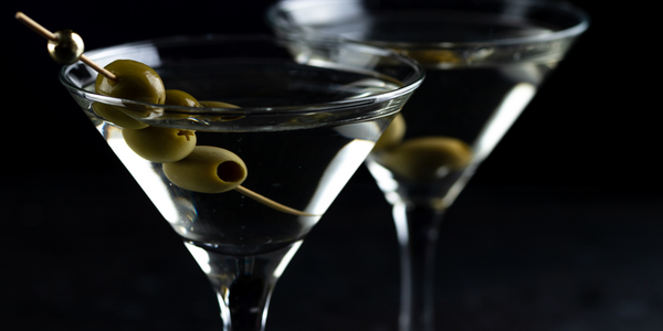 Two gin martinis against a black background with three olives each