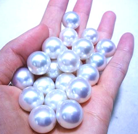 Une vingtaine de perles blanches argentées de 16-17mm dans une main.
