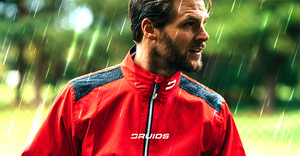 A man wearing a vibrant red Druids waterproof golf jacket with shoulder reinforcements stands in the rain, showcasing the jacket's durability and style as part of Druids' anticipated golf rain gear collection for 2023.