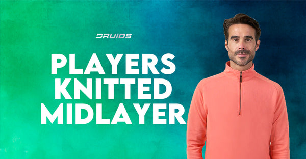 A man wearing Druids' knitted midlayer in salmon pink with a zip neck, displayed with 'PLAYERS KNITTED MIDLAYER' in bold white font, against a teal and blue watercolor background.