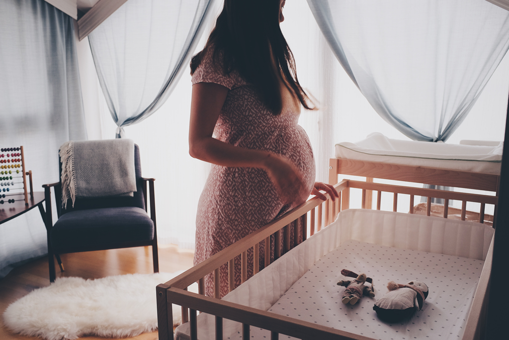 A woman standing beside a baby cot bed