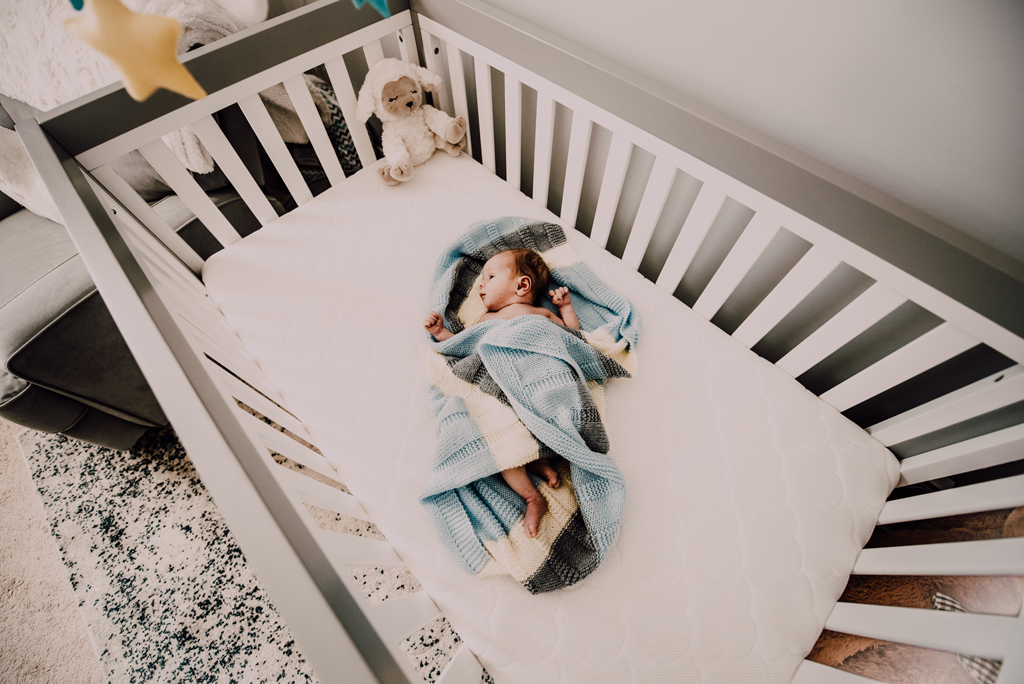 Baby wrapped in blue blanket in the crib 