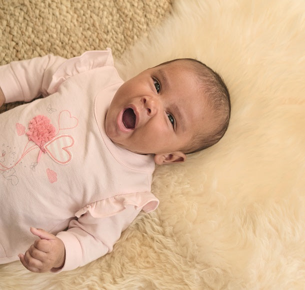 Little baby wear a pink sleepsuit is yawning