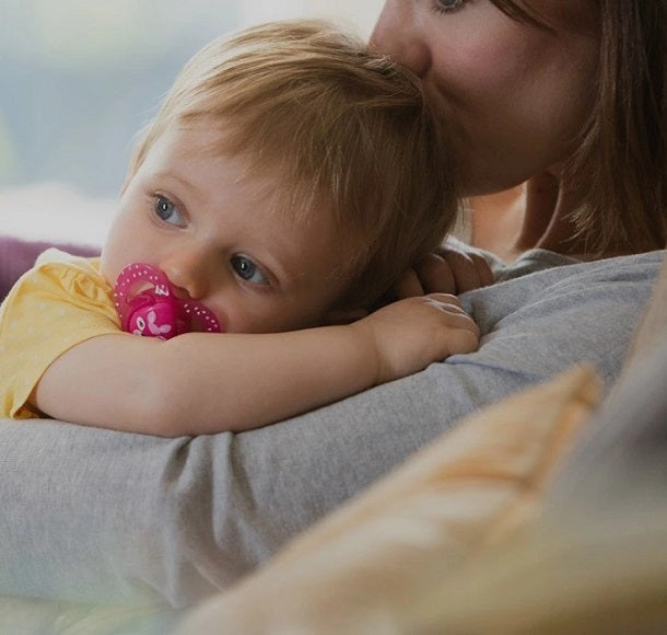 Baby boy with a soother is hugging his mother