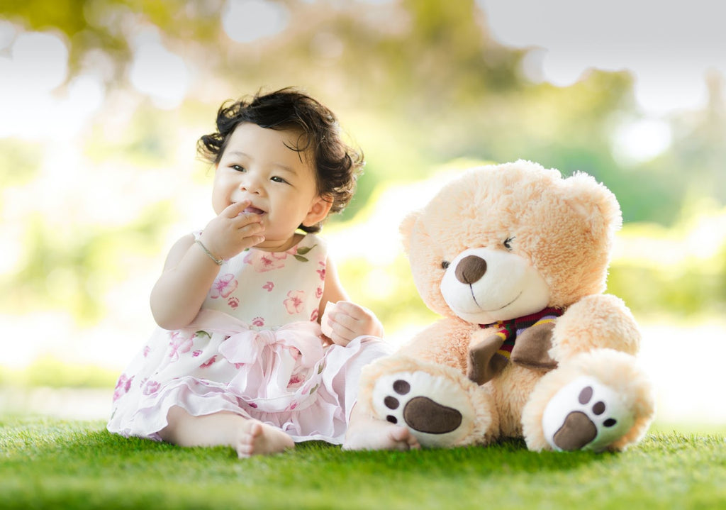 Baby girl sitting on green grass with a plush bear