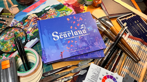Photo of three copies of the Scarland Artbook amongst a variety of suplies including paint brushes, paint knives, painter's tape, traditional ink pens, pencils, and notebooks.  One book is open to show the map of Scarland, and the other two are stacked in the center.