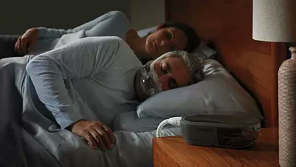 couples sleeping on bed next to each other with Philips Respironics cpap mask and machine taking sleep apnae treatment