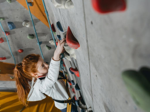 Kind mit roten langen Haaren auf Kletterwand