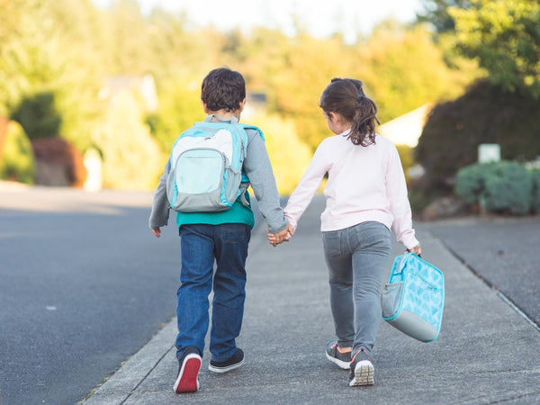 Zwei Kinder, Bild von hinten, gemeinsam am Schulweg, Hände haltend