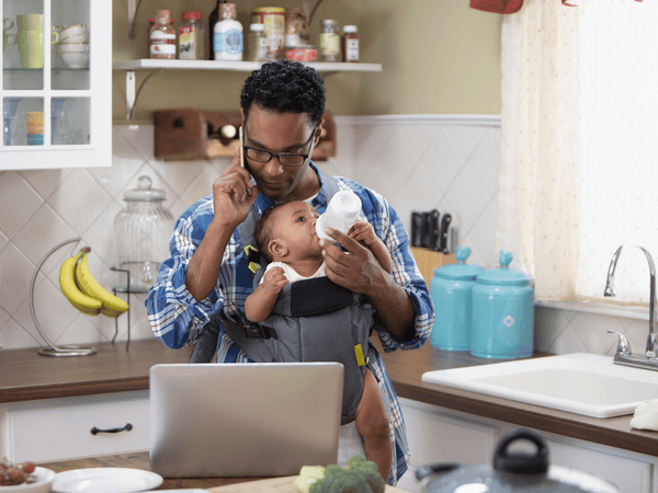 Working Dad: Am Handy mit Milchflasche in der anderen Hand und Blick auf den Laptop