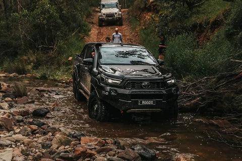Cara driving her black 4wd Toyota Hilux on a rocky river. 