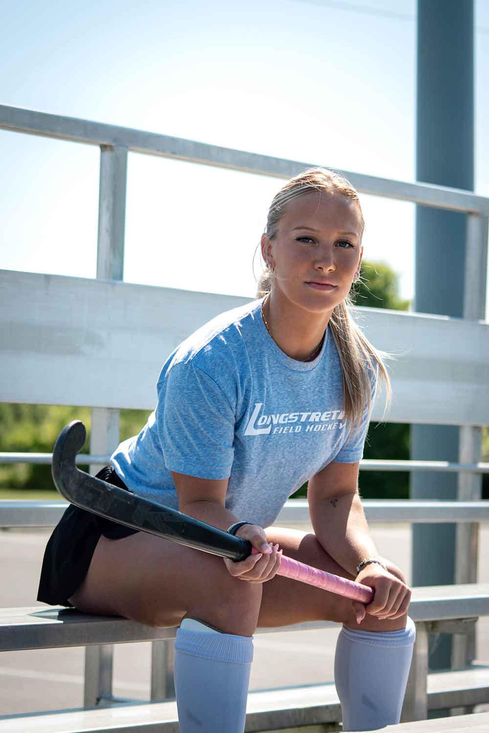 Field hockey player Sophia sitting on a bench holding a stick.