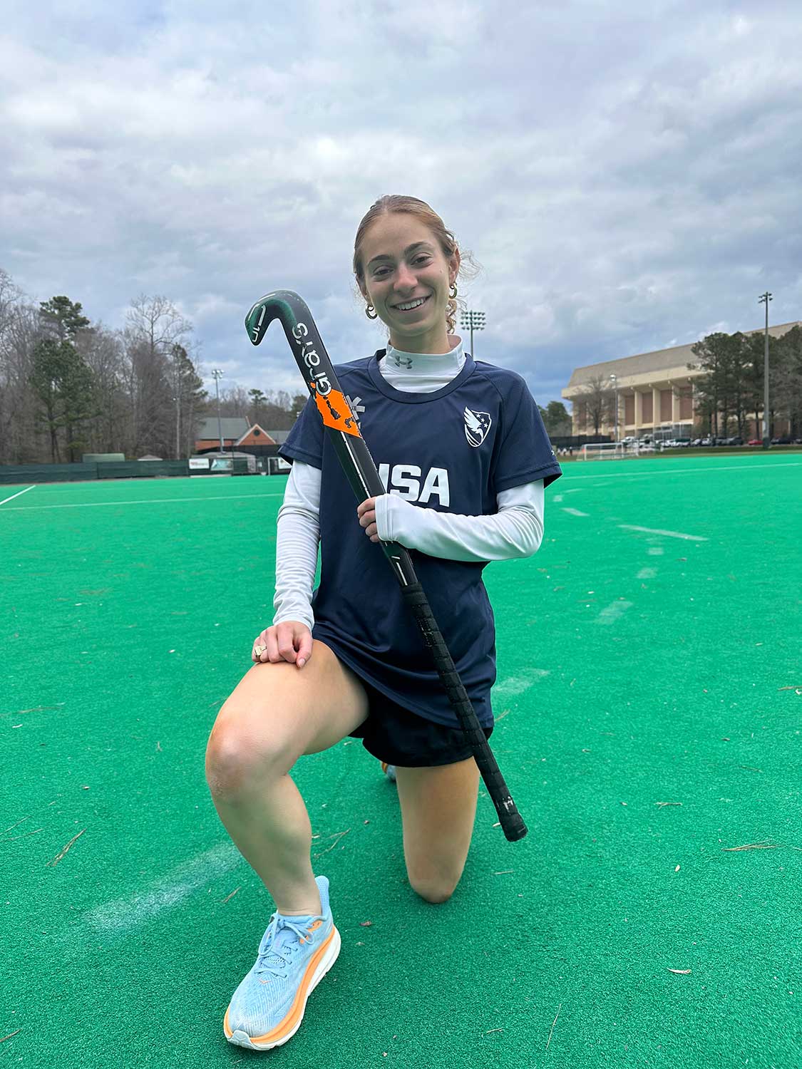 Field hockey player kneeling on the field holding a stick.